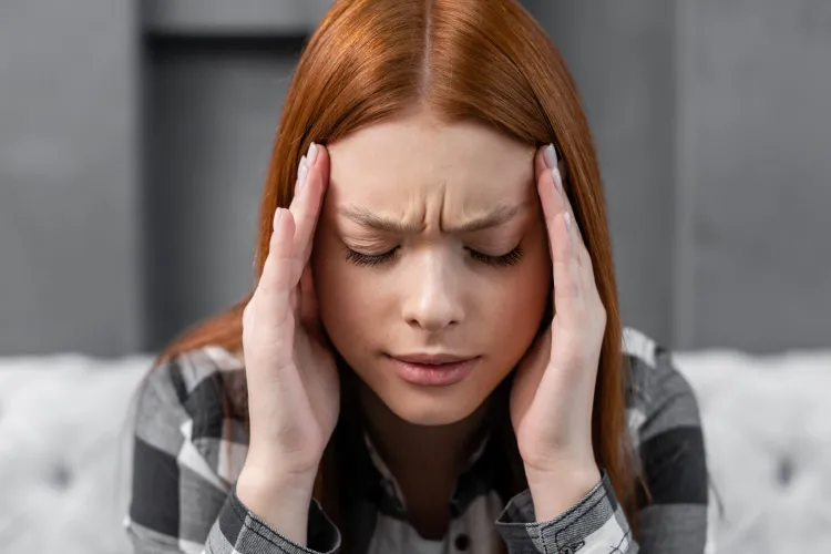 a woman is sitting and suffering from a migraine